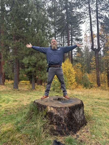 Adam Mayer standing on a tree stump with arms wide open